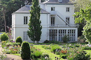 Maison de maître aux façades blanches avec l'iriseraie au premier plan.