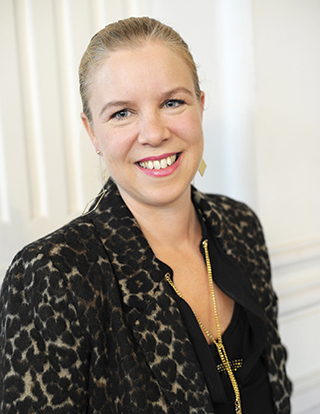 Une femme blonde souriante, vêtue d'une veste sombre aux motifs tâchetés.